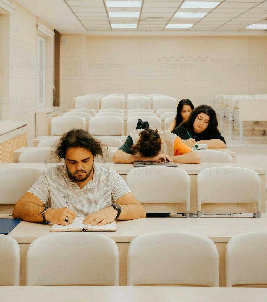 Students in a classroom, some appearing tired, with one student resting on their desk.