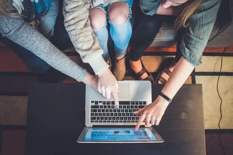 Three people pointing at a laptop screen while sitting together on a couch.