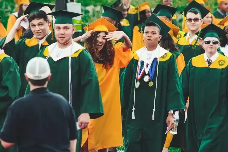 Students in green and gold graduation gowns celebrating at a ceremony.