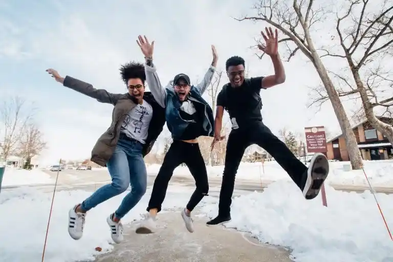 Three college students jumping joyfully outdoors on a snowy day.