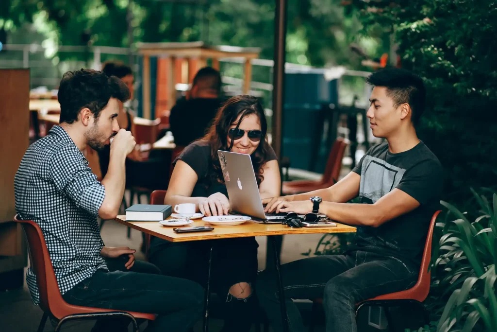 Three students collaborating on a project while sitting at an outdoor cafe.