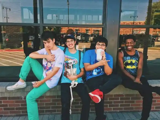 A group of four diverse college students sitting on a bench outside a building, smiling and enjoying their time together.