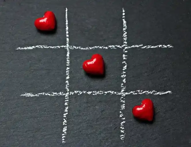 Tic-tac-toe game with red heart-shaped pieces on a black chalkboard.